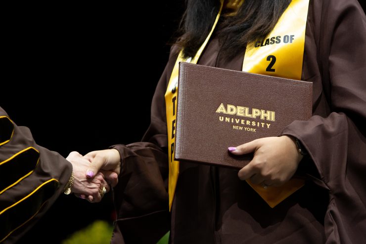 Graduate holding diploma while shaking hands during  graduation ceremony