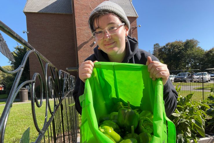 A proud student volunteer showing the bountiful harvest of bell peppers from the  community garden.