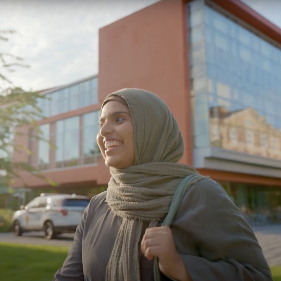 An student smiling and walking in front of the Nexus building.