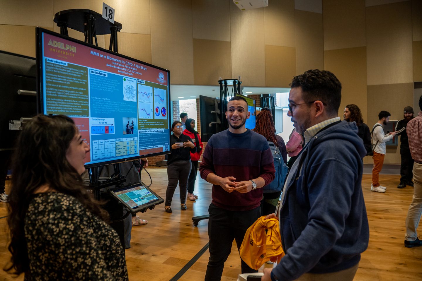 Three students standing by an e-poster discuss a 2023 Research Day presentation on biomarkers in the University Center.
